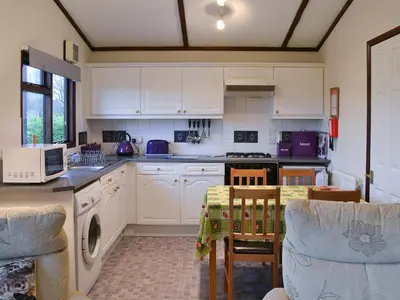 a kitchen with white cabinets and a table and chairs at Catbank in Bridekirk
