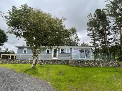 a blue house with a tree in the grass at Swallows Lodge in Keswick