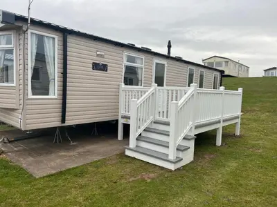 a mobile home with a white staircase and grass at Robinson retreats beautiful caravan with sea views pet friendly in Mainsriddle