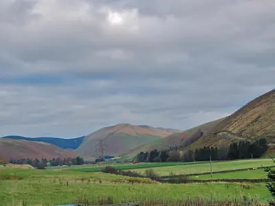 a view of a field with mountains in the background at Ewes Schoolhouse in Bentpath