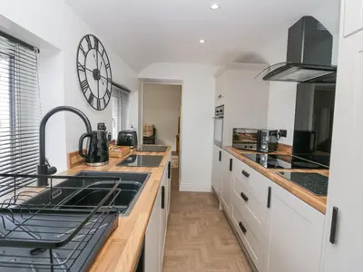 a kitchen with white cabinets and a clock on the wall at Victroneen Cottage in Whitehaven