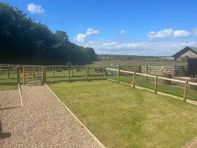a wooden fence in a field with animals in the distance at Millburn Mini Farm in Kilwinning
