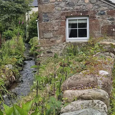 a stone house with a window and a stream at Annie's Cottage in Gosforth