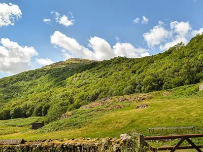 a green hillside with a wooden fence on it at Church House in Ulpha