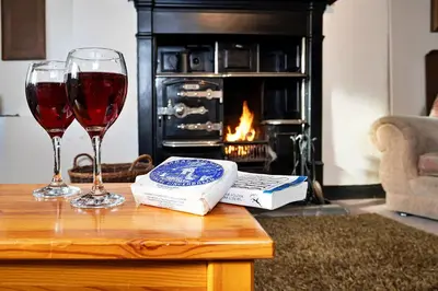 two glasses of wine on a table with a fireplace at Finest Retreats - Town Head Cottage in Grasmere in Grasmere