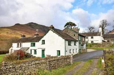 a white house with green windows and a stone wall at Finest Retreats - Town Head Cottage in Grasmere in Grasmere