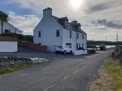 a white house with a car parked in front of it at The Old Cornstore a beautiful Suite overlooking the sea in Drummore