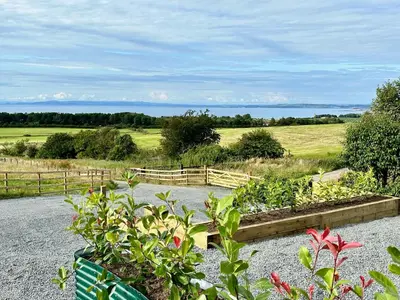 a garden with a view of a field and the ocean at Firth View 1 - Luxury Cottage with Sea View & Hot Tub, Ayr in Ayr