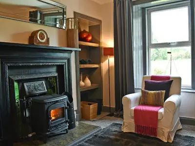 a living room with a wood stove and a chair at 2 Northbank Cottages in Whiting Bay