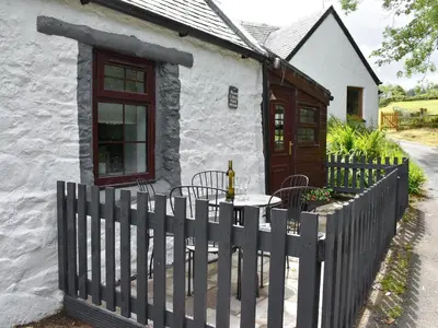 a white cottage with a wooden fence and a table at Ivy Cottage in Whiting Bay