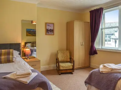 a bedroom with two beds and a chair and a window at Cumberland Place in Keswick