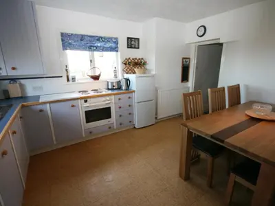 a kitchen with white cabinets and a table and a dining room at East Cottage in Mainsriddle