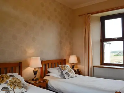 two beds in a bedroom with two lamps and a window at Allanhead in Borgue