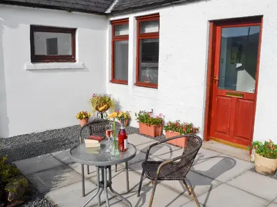 a patio with a table and chairs and a red door at Beuchan Cottage Keir Mill in Closeburn