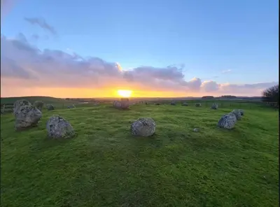 a field with large rocks in a field with the sunset at Large country house with garden, outdoor spa area & games room with Hot Tub and Fire Pit in Wigtown