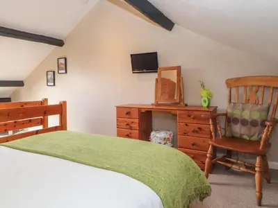 a bedroom with a bed and a chair and a dresser at Lillibet Cottage in Keswick