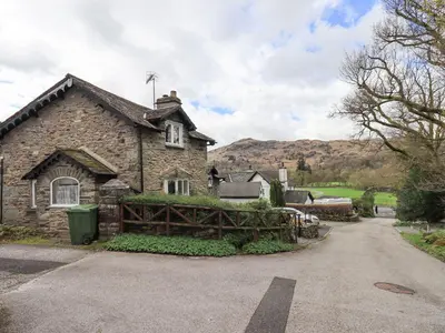 a stone house with a fence next to a road at Hollens Cottage in Ambleside