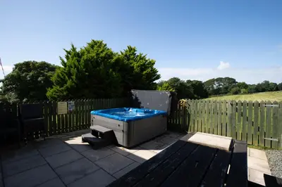a hot tub sitting on a patio next to a fence at Auchenlarie Courtyard No 1 in Gatehouse of Fleet