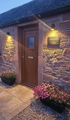 a stone building with a wooden door and some flowers at Country cottage with garden, views & games room in Dumfries