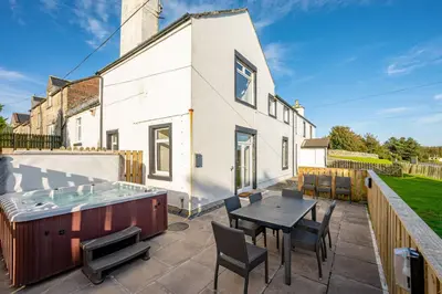 a patio with a table and chairs and a hot tub at Auchenlarie Farmhouse in Gatehouse of Fleet
