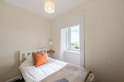 a bedroom with a bed with an orange pillow and a window at Auchenlarie Farmhouse in Gatehouse of Fleet