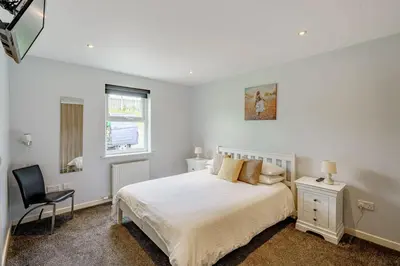 a white bedroom with a bed and a chair at Auchenlarie Courtyard No 4 in Gatehouse of Fleet
