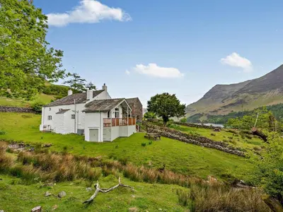 a white house on a green hill with mountains in the background at 4 Bed in Buttermere oc-sz090 in Buttermere