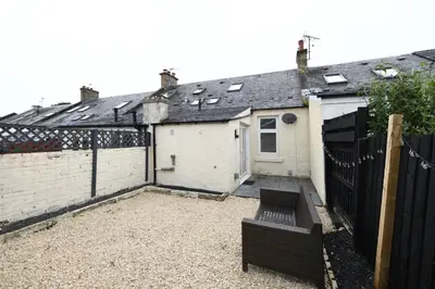 a small white house with a black fence at Hunter Links Cottage in Prestwick