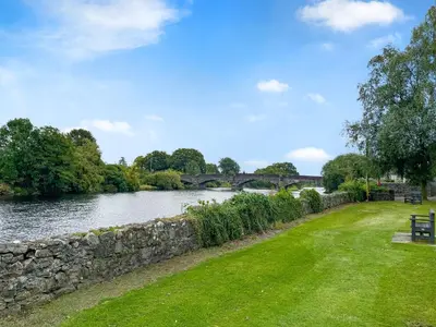 a river with a stone wall and a bridge at Peppy in Newton Stewart