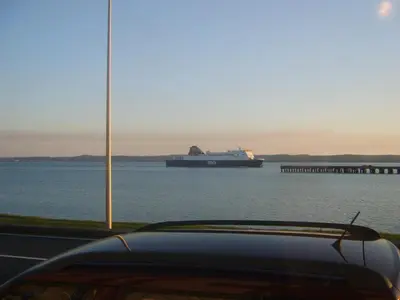 a car parked next to a large ship in the water at The Merchants House in Cairnryan