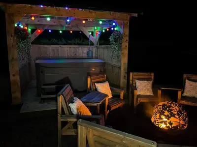 a porch with chairs and a fireplace with lights at Bungalow with Hot Tub, BBQ Hut, Golf Net , Large Garden & Play Area in Maybole