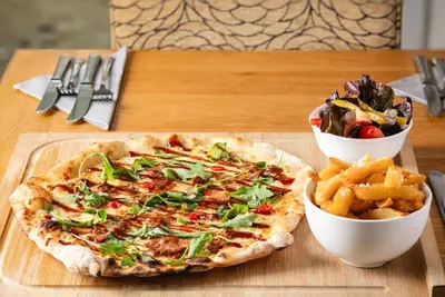 a pizza and a bowl of fries on a table at The Kellbank in Gosforth