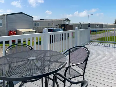 a table and chairs on a deck with a fence at Bud's Bay in Mainsriddle
