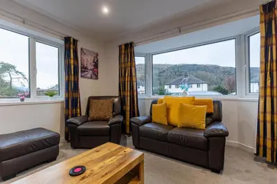 a living room with two chairs and a table and windows at SHELTER STONE - Cottage in the heart of the Lakes in Keswick