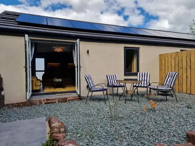 a patio with chairs and a table in front of a house at The Stables by Blake View Holidays, comprising The Nest, The Drey, The Burrow and the Den, 3 miles from Ennerdale in Rowrah