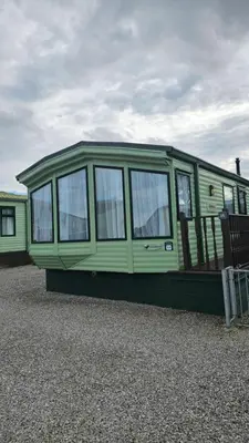 a green mobile home sitting on top of gravel at The Lake District Caravan in Lamplugh