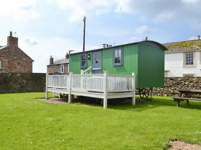 a green house with a porch and a bench at Hannah's Shepherds Hut - Uk43564 in Bowness-on-Solway