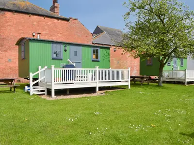 a green building with a white fence in a yard at Ryan's Shepherd Hut - Uk43565 in Bowness-on-Solway