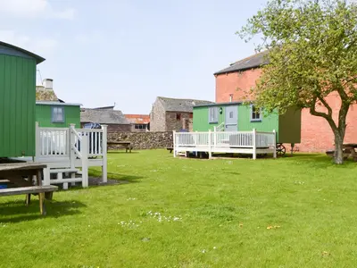 a group of houses in a grassy yard with a bench at Ryan's Shepherd Hut - Uk43565 in Bowness-on-Solway