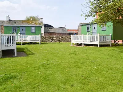 a yard with green houses and a white fence at Ryan's Shepherd Hut - Uk43565 in Bowness-on-Solway