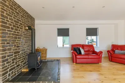 a living room with two red chairs and a brick fireplace at The Stables at Brickrow Farm in Ayr