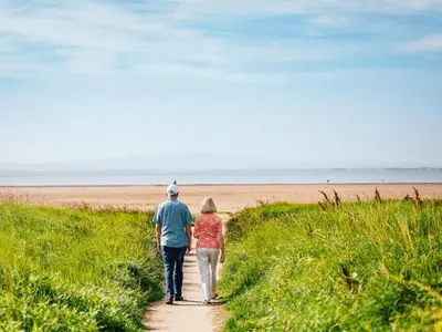 a man and woman walking down a path towards the beach at Queensberry Bay Essential Clover Caravan Pet in Annan