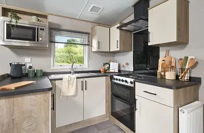 a kitchen with white cabinets and a stove top oven at Queensberry Bay Essential Clover Caravan in Annan