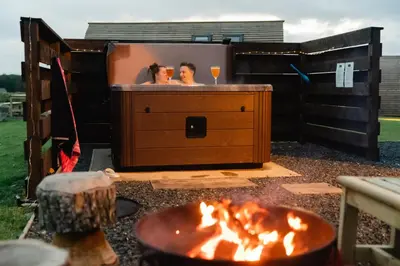 two people in a bath tub with a fire pit at Wigtown by Wigwam Holidays in Newton Stewart