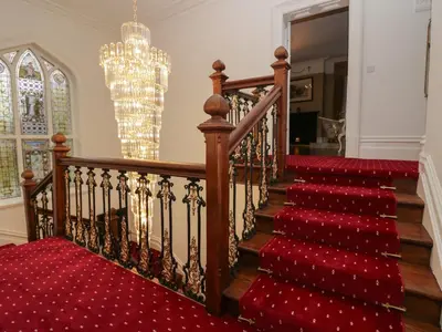 a staircase with a red carpet and a chandelier at Beechgrove Manor in Workington