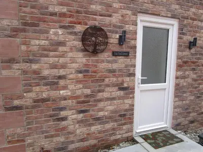 a brick wall with a white door and a window at Oak End Stay in Carlisle