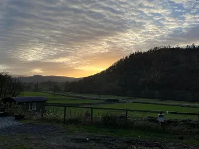 a sunset over a field with a fence and a hill at The Shepherd's Nook in Thirlmere