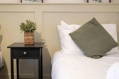 a bed with a pillow and a table with a plant on it at The Fairlie Suite No2 in Prestwick
