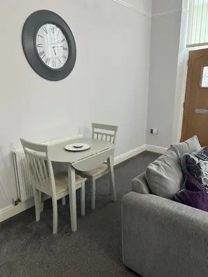 a living room with a table and a clock on the wall at 10 Thurnams House in Carlisle
