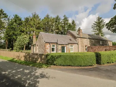 an old brick house with a fence and bushes at Waterside Lodge in Lockerbie